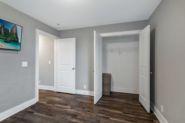 unfurnished bedroom featuring dark wood-style floors, a closet, and baseboards