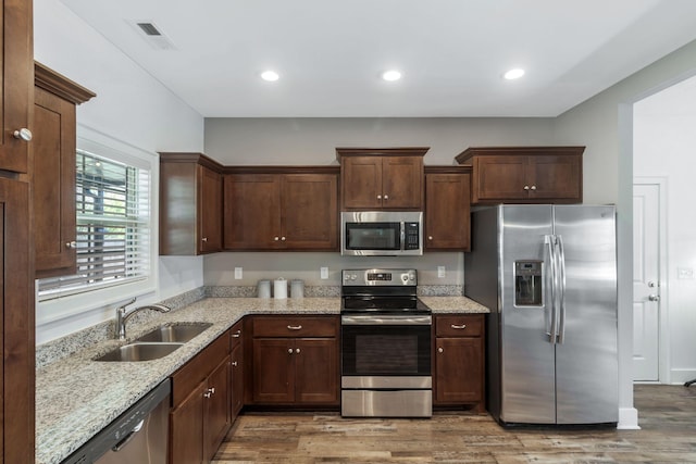 kitchen featuring visible vents, light wood-style flooring, a sink, light stone counters, and appliances with stainless steel finishes