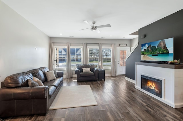 living room with a ceiling fan, baseboards, recessed lighting, a lit fireplace, and dark wood-type flooring