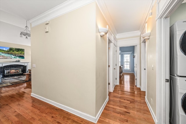 hall featuring stacked washer and clothes dryer, baseboards, light wood-style floors, and ornamental molding