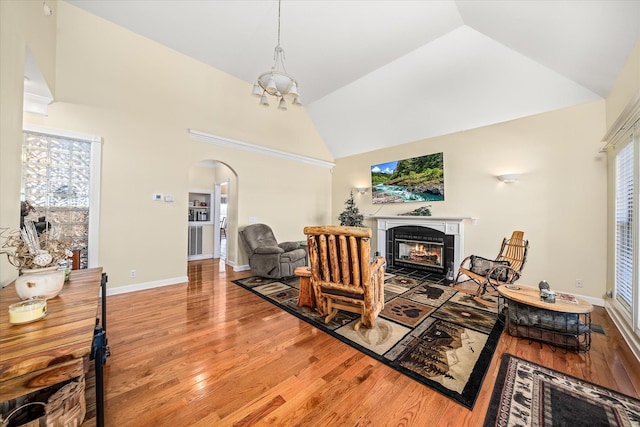 living area with high vaulted ceiling, light wood-style flooring, a tiled fireplace, arched walkways, and baseboards