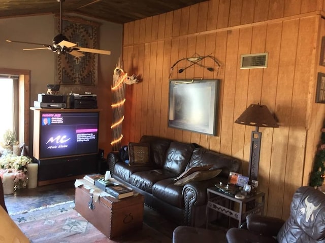 living room featuring visible vents, wooden walls, and a ceiling fan