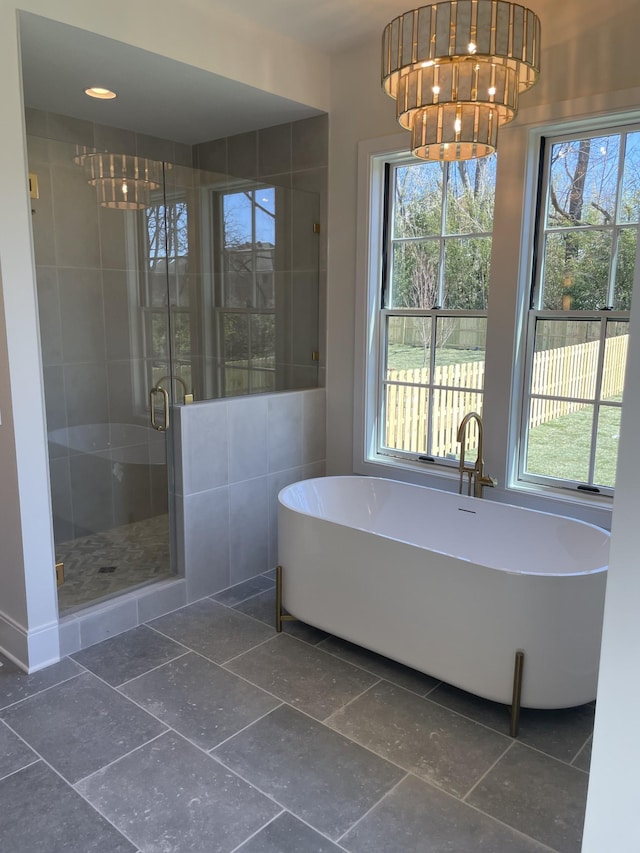 bathroom with a wealth of natural light, a shower stall, a freestanding bath, and an inviting chandelier