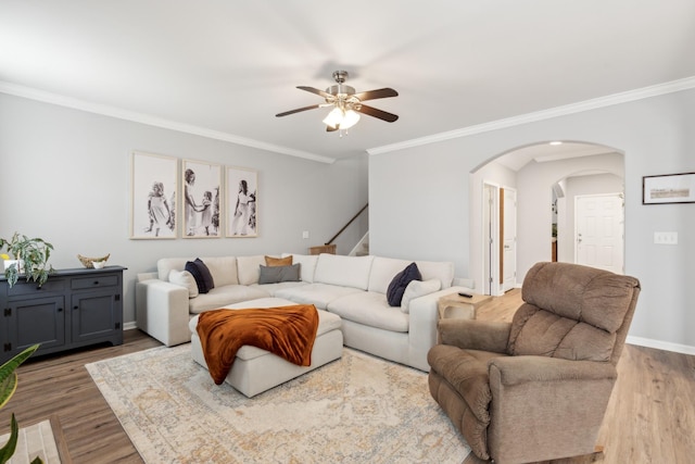 living room featuring wood finished floors, baseboards, arched walkways, ceiling fan, and crown molding