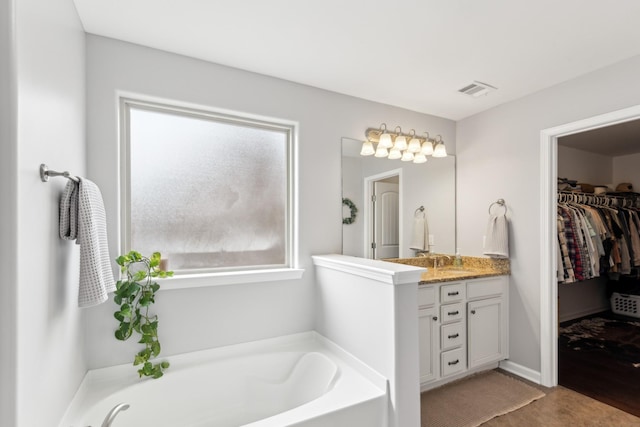 bathroom featuring visible vents, a garden tub, a walk in closet, and vanity