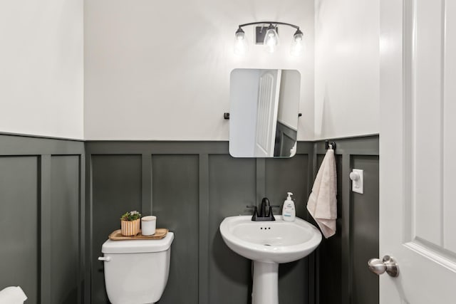 bathroom featuring a decorative wall, toilet, a wainscoted wall, and a sink