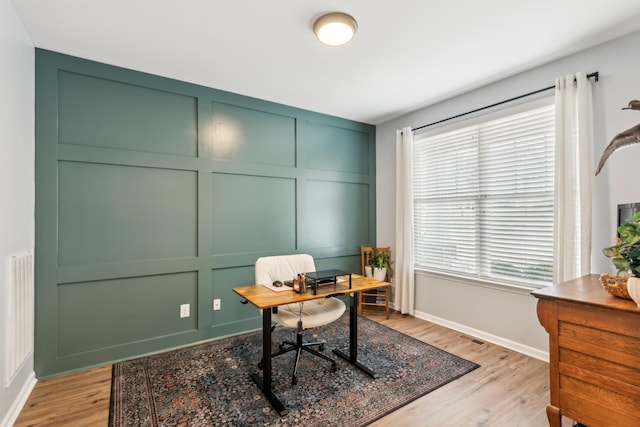 office featuring a decorative wall, baseboards, and light wood finished floors