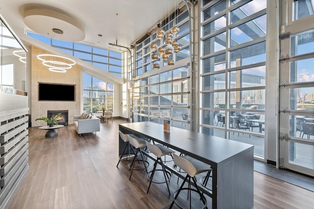 dining area featuring a towering ceiling, expansive windows, wood finished floors, and a tiled fireplace