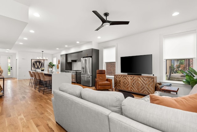 living area with recessed lighting, light wood-style flooring, ceiling fan with notable chandelier, and baseboards