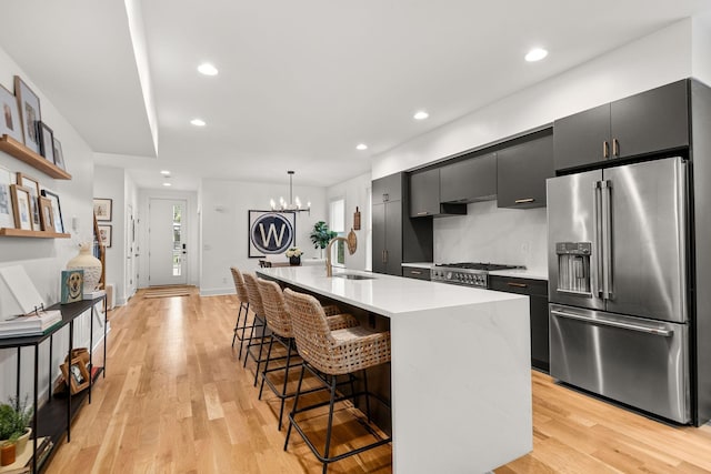 kitchen featuring a sink, a kitchen breakfast bar, light countertops, dark cabinets, and high end refrigerator