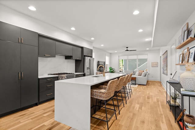 kitchen featuring a breakfast bar area, a kitchen island with sink, a sink, light countertops, and light wood-style floors