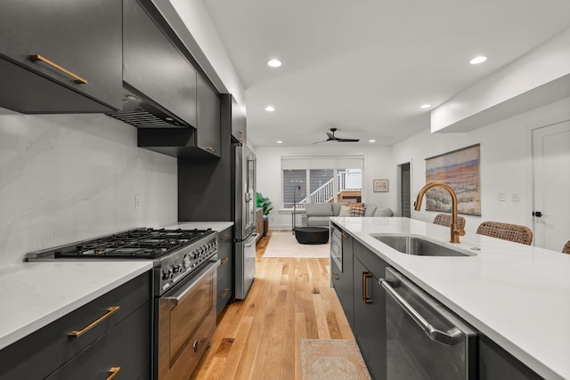 kitchen with light wood finished floors, a sink, light countertops, premium appliances, and dark cabinets