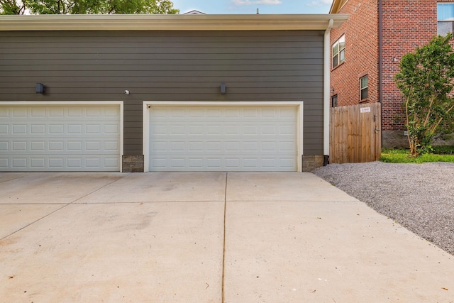 garage featuring concrete driveway and fence