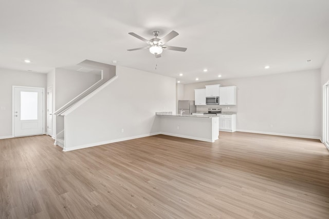 unfurnished living room with stairs, recessed lighting, baseboards, and light wood finished floors