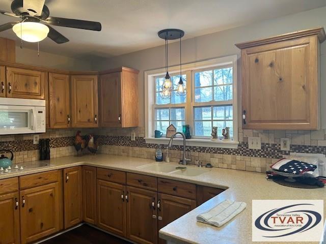 kitchen with a sink, decorative light fixtures, backsplash, light countertops, and white microwave