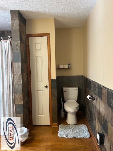 bathroom featuring toilet, tile walls, wood finished floors, and a textured ceiling