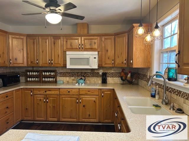 kitchen with white microwave, a sink, light countertops, pendant lighting, and tasteful backsplash