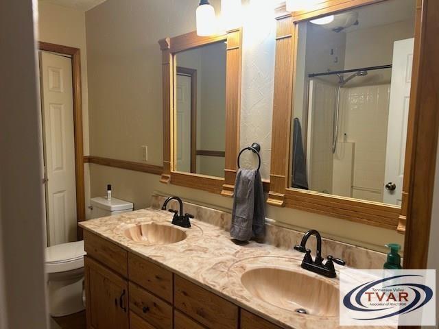 bathroom featuring double vanity, toilet, walk in shower, and a sink