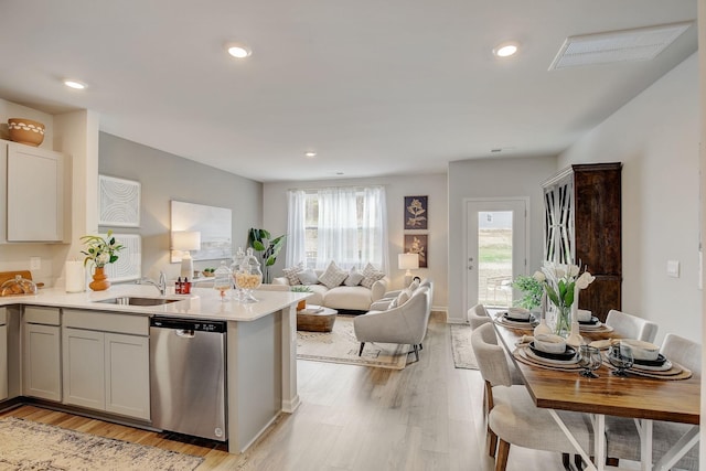 kitchen featuring a peninsula, light wood-style flooring, a sink, stainless steel dishwasher, and open floor plan