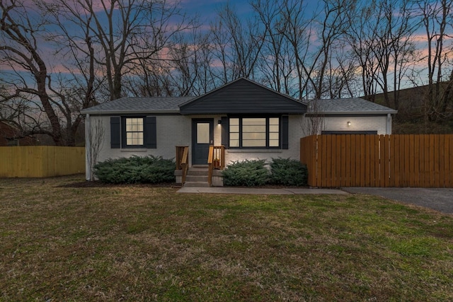 view of front of house featuring fence, brick siding, driveway, and a lawn