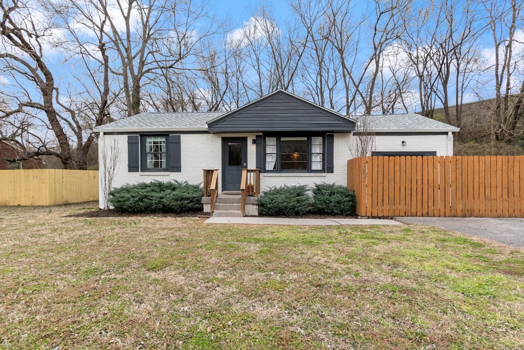 bungalow with a front yard, fence, brick siding, and a shingled roof