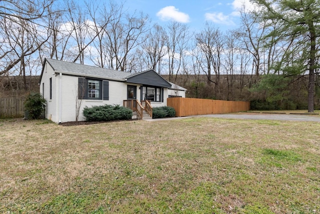 view of front of house with a front yard, fence, brick siding, and roof with shingles