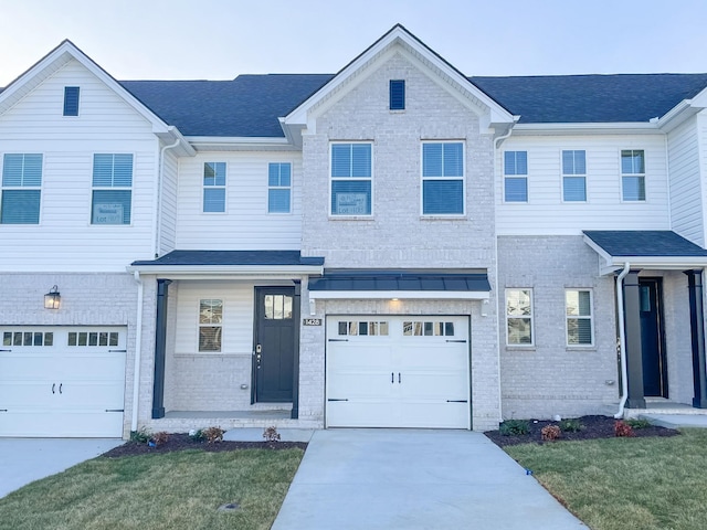 townhome / multi-family property featuring a front lawn, concrete driveway, a shingled roof, a garage, and brick siding