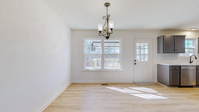 unfurnished dining area featuring light wood finished floors, an inviting chandelier, baseboards, and a sink