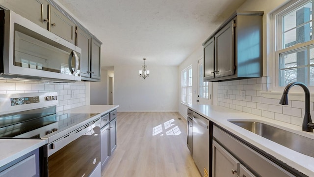 kitchen with gray cabinets, a sink, light countertops, light wood-style floors, and appliances with stainless steel finishes