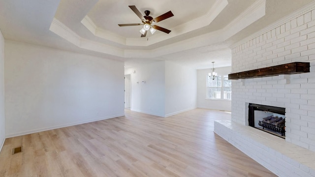 unfurnished living room with a tray ceiling, a brick fireplace, light wood finished floors, and ornamental molding