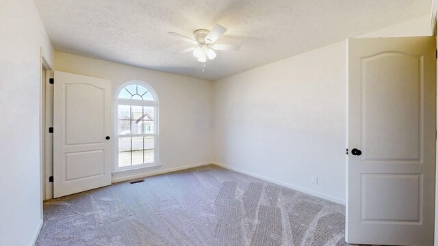 carpeted empty room featuring a textured ceiling, visible vents, baseboards, and ceiling fan