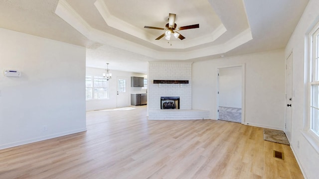 unfurnished living room with light wood finished floors, visible vents, a brick fireplace, crown molding, and a raised ceiling