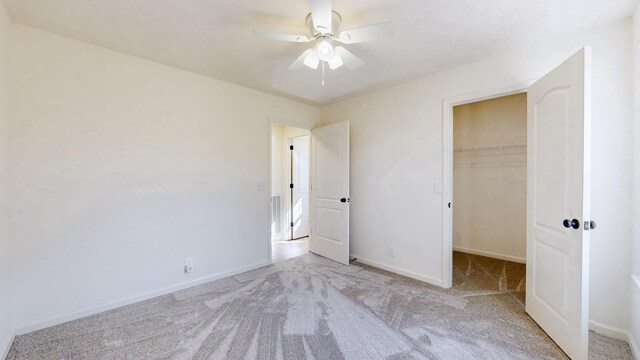 unfurnished bedroom with a spacious closet, ceiling fan, baseboards, carpet, and a closet