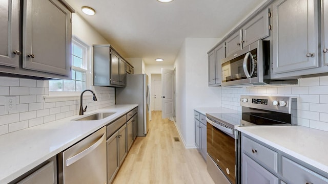 kitchen with light wood finished floors, gray cabinets, appliances with stainless steel finishes, and a sink