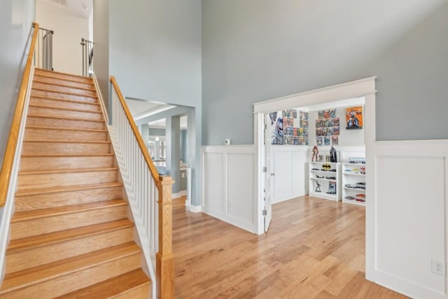 staircase with a decorative wall, wainscoting, a towering ceiling, and wood finished floors