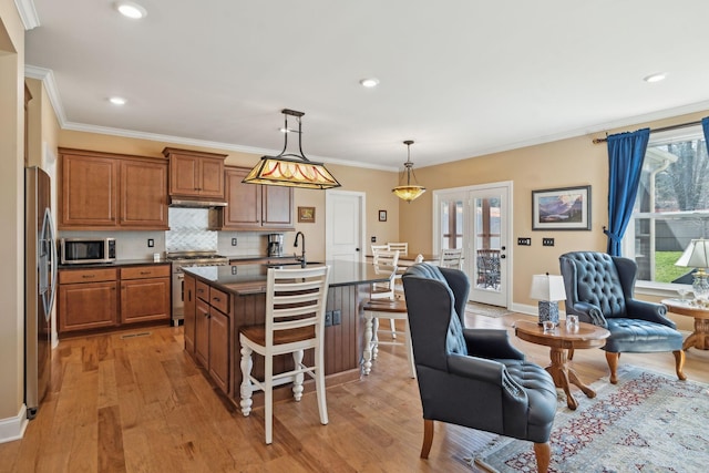 kitchen with light wood-type flooring, dark countertops, appliances with stainless steel finishes, and brown cabinetry