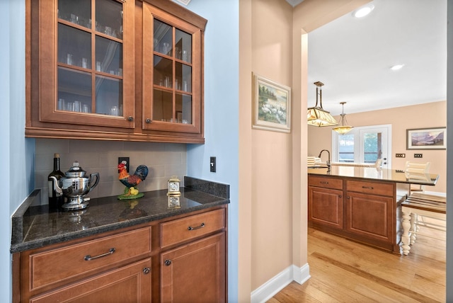 bar with decorative light fixtures, light wood-type flooring, baseboards, and tasteful backsplash