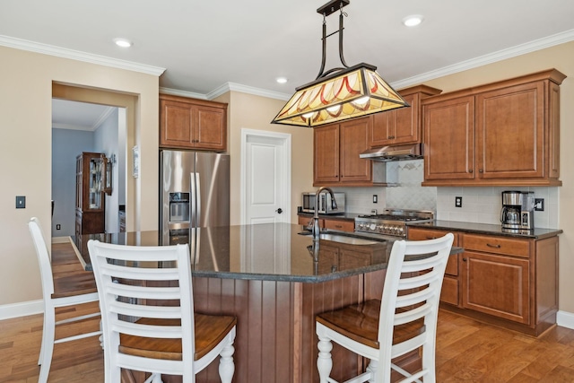 kitchen featuring light wood-type flooring, ornamental molding, under cabinet range hood, appliances with stainless steel finishes, and decorative backsplash