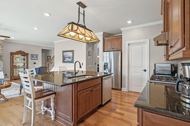 kitchen featuring a sink, under cabinet range hood, a kitchen breakfast bar, light wood-style flooring, and appliances with stainless steel finishes