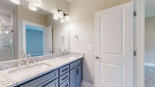 bathroom featuring double vanity, a tile shower, baseboards, and a sink