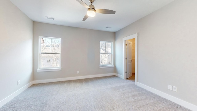 carpeted spare room with visible vents, baseboards, a healthy amount of sunlight, and a ceiling fan