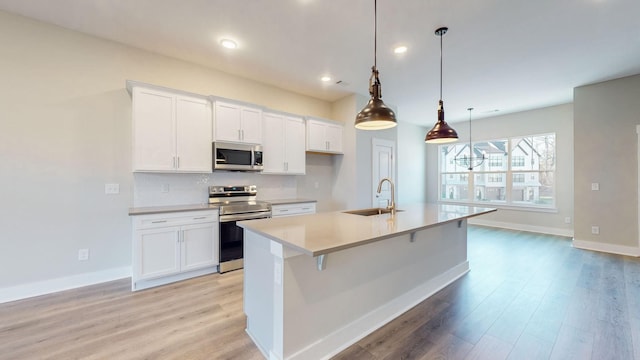 kitchen featuring light wood-style flooring, a sink, tasteful backsplash, white cabinetry, and appliances with stainless steel finishes