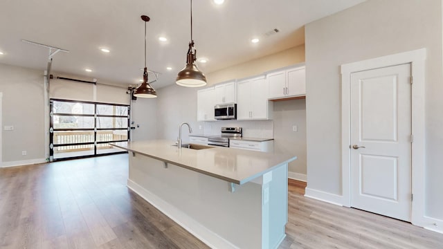 kitchen featuring an island with sink, a sink, light wood-style floors, appliances with stainless steel finishes, and white cabinetry