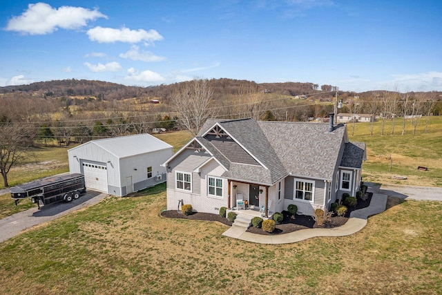 view of front of home with a shingled roof, a front lawn, covered porch, an outdoor structure, and driveway