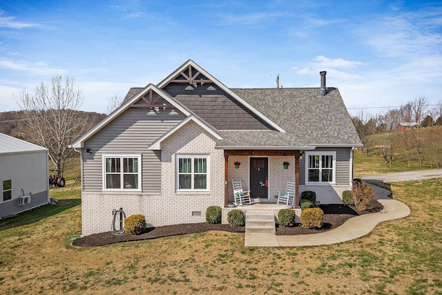 view of front facade featuring brick siding, covered porch, a front lawn, and roof with shingles