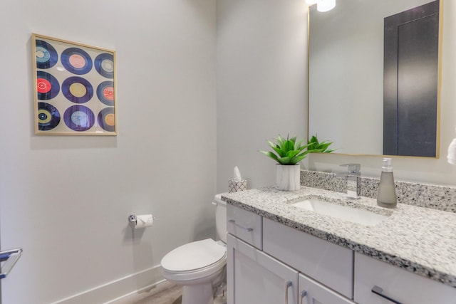 half bath with baseboards, toilet, and vanity