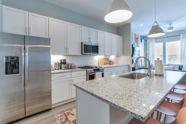 kitchen featuring a sink, stainless steel appliances, a kitchen breakfast bar, light wood-type flooring, and backsplash