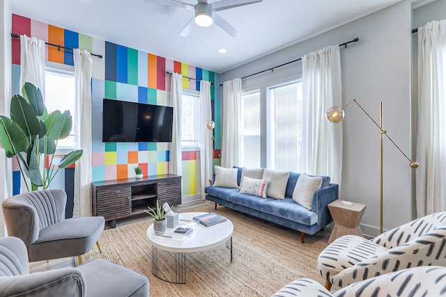 living room featuring wallpapered walls, an accent wall, baseboards, and ceiling fan