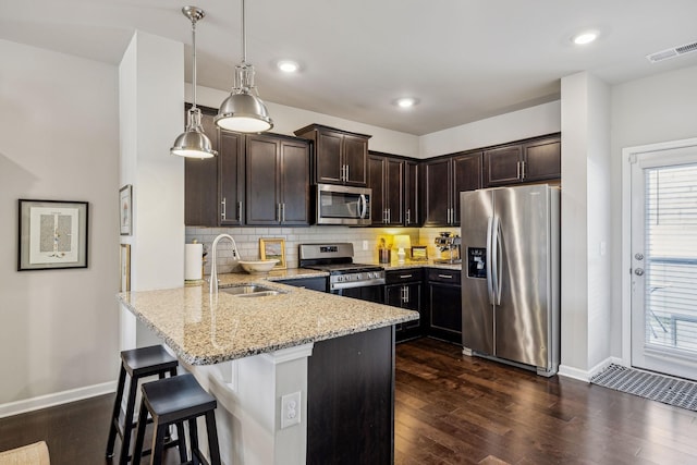 kitchen featuring visible vents, a sink, light stone counters, appliances with stainless steel finishes, and a peninsula