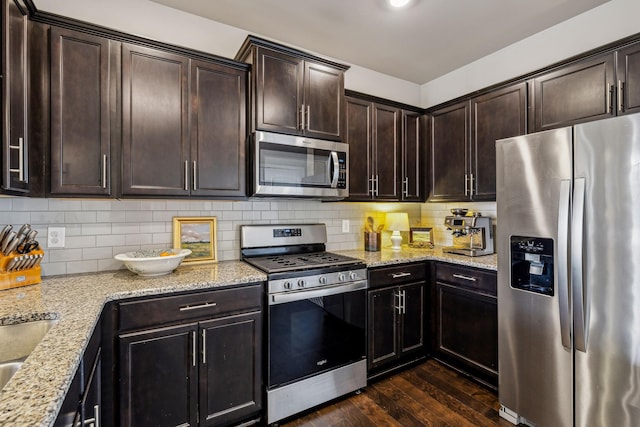 kitchen with light stone counters, dark wood-style flooring, decorative backsplash, dark brown cabinetry, and appliances with stainless steel finishes